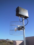 9/2002: A Wi-Fi bridge with parabolic mesh antenna. The ammo box enclosed a D-Link access point and power-over-ethernet splitter. I bridged a link just under a mile long with two units like this.